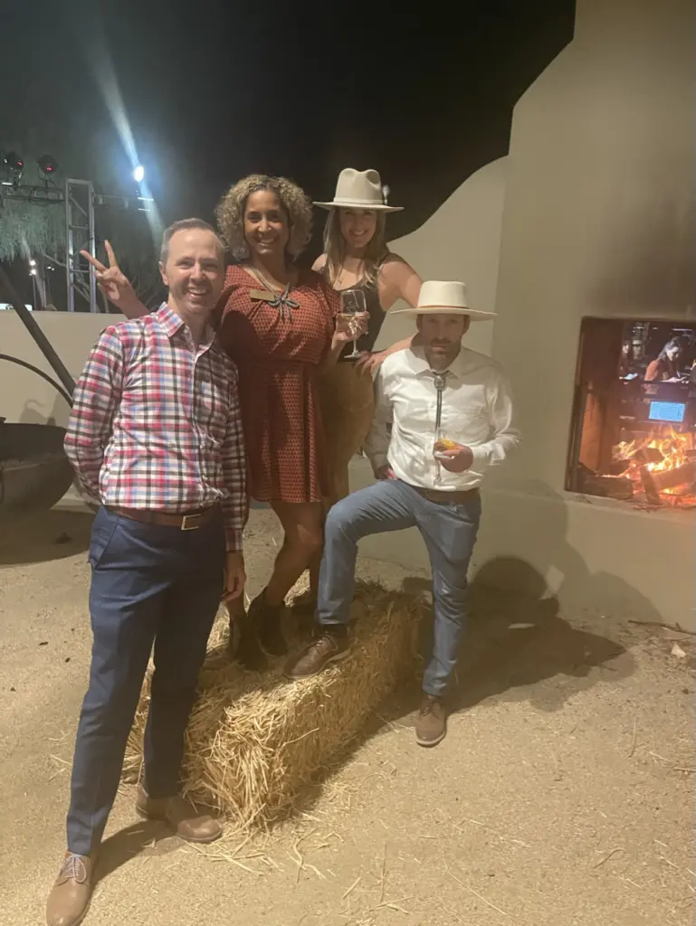 Group posing near outdoor fireplace, wearing hats.