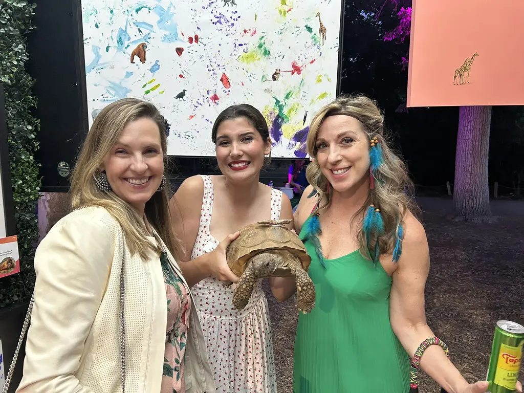 Three women smiling, holding a turtle.