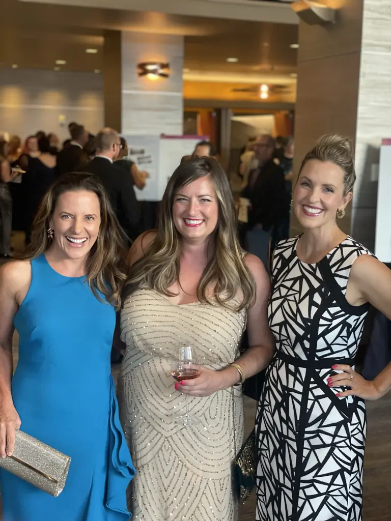 Three women smiling at formal event.