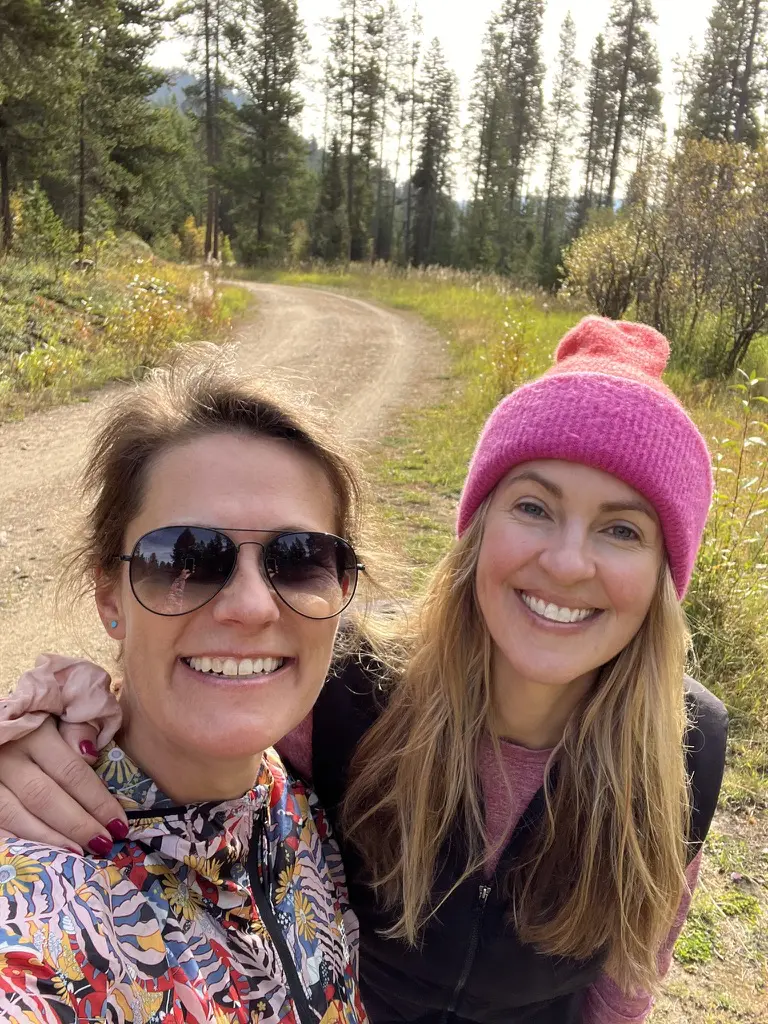 Two women smiling on a forest trail.