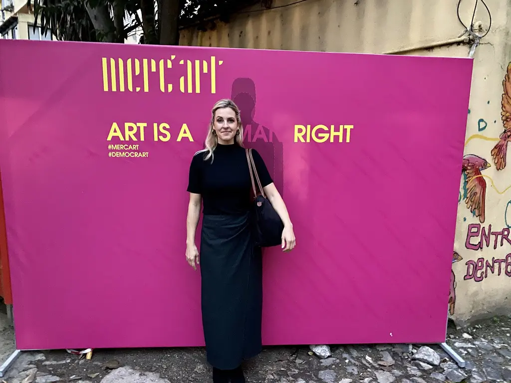 Woman standing by pink "Art is a" sign.