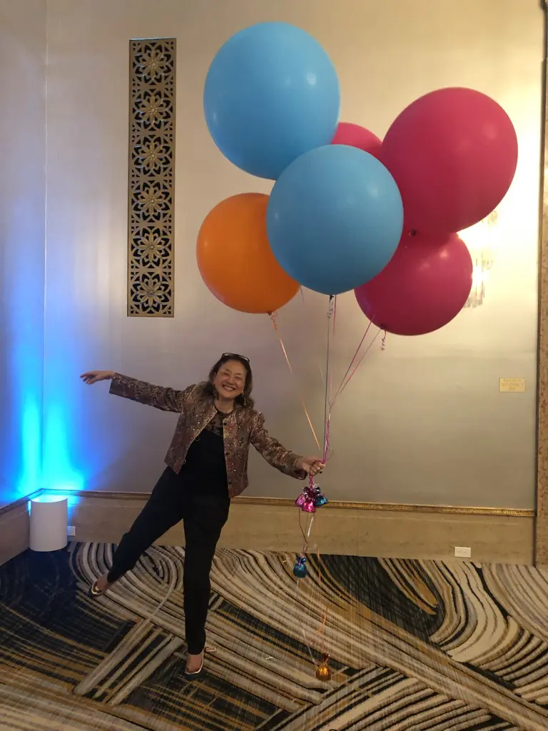 Person joyfully holding large colorful balloons indoors.