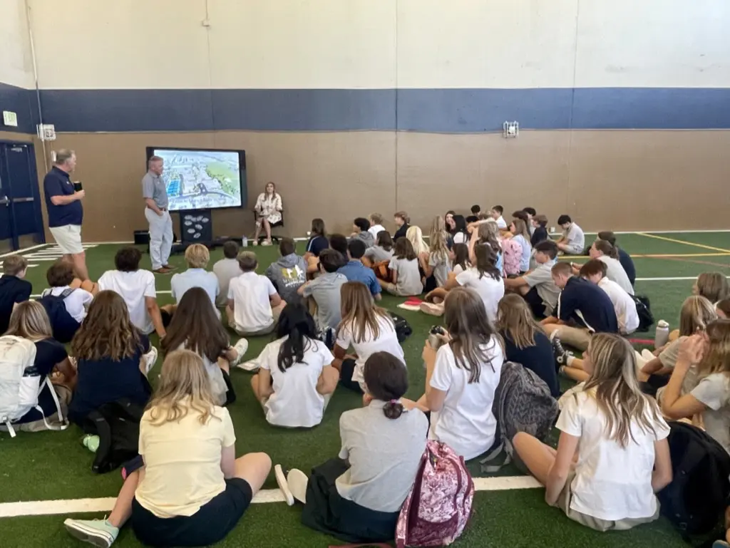 Students seated on gym floor listening attentively.