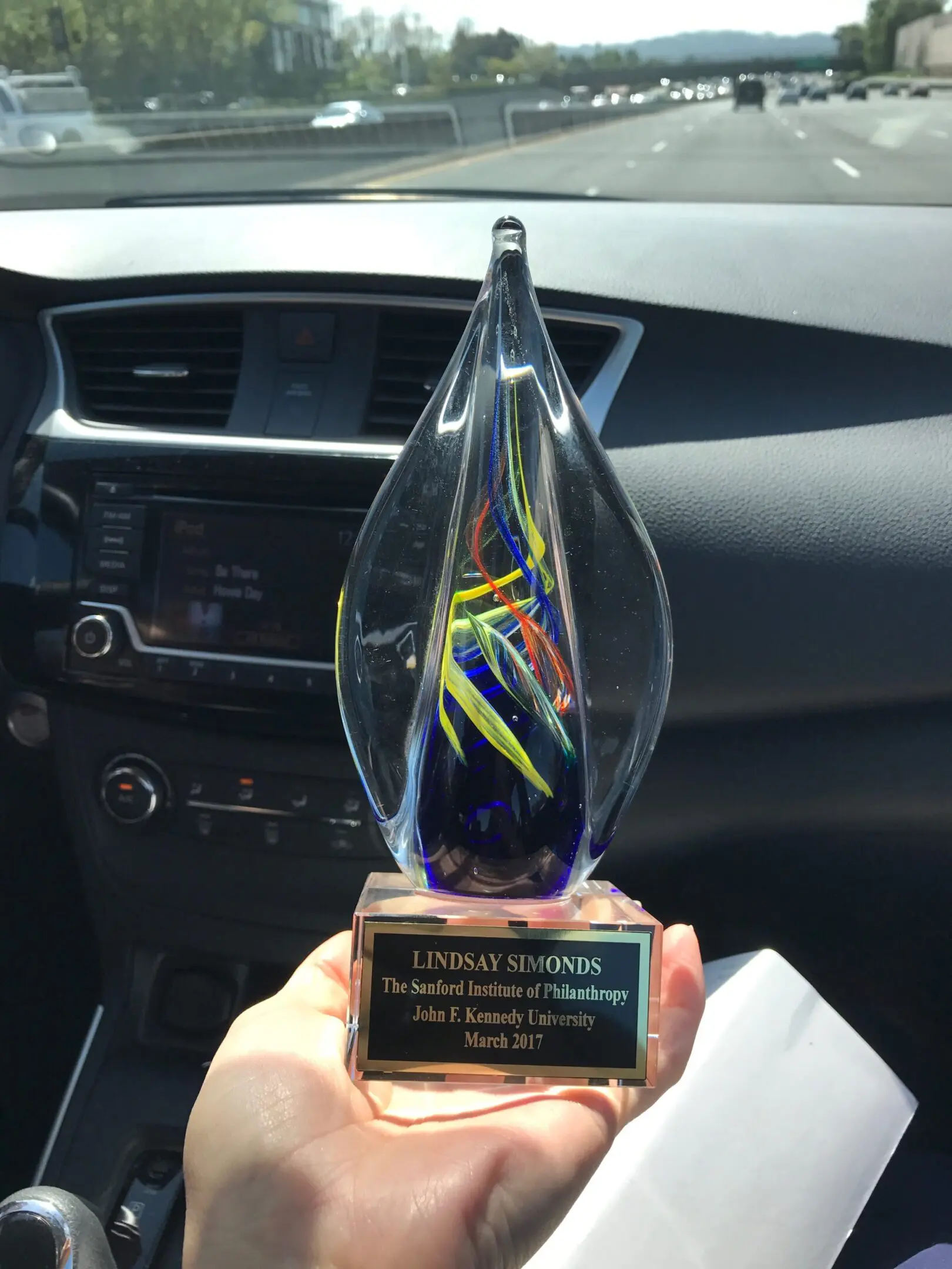 Hand holding colorful glass award in car.