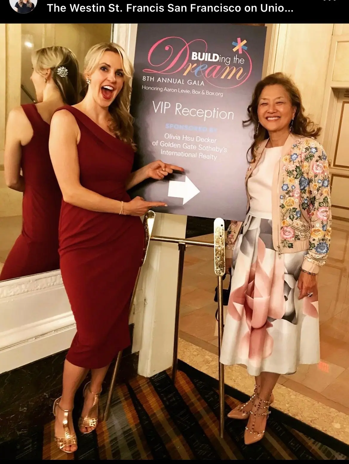 Two women standing near event sign.